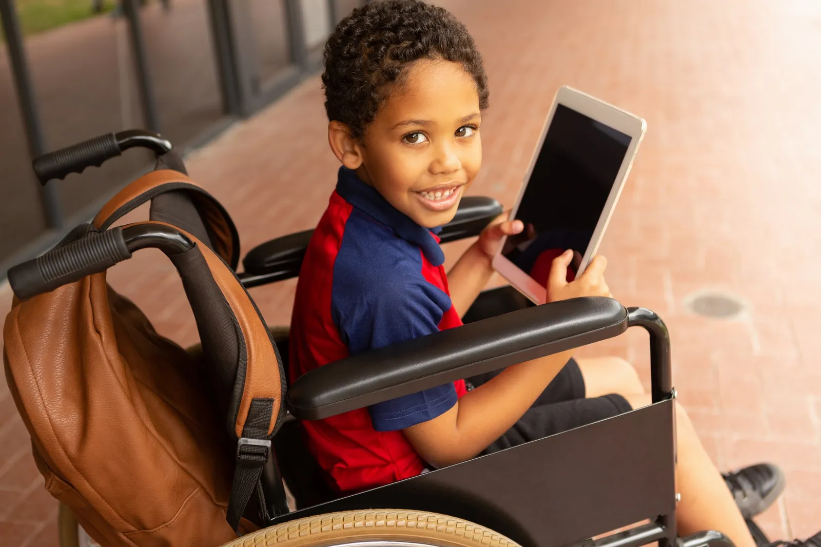 Disabled schoolboy with digital tablet looking at camera in corridor at elementary school